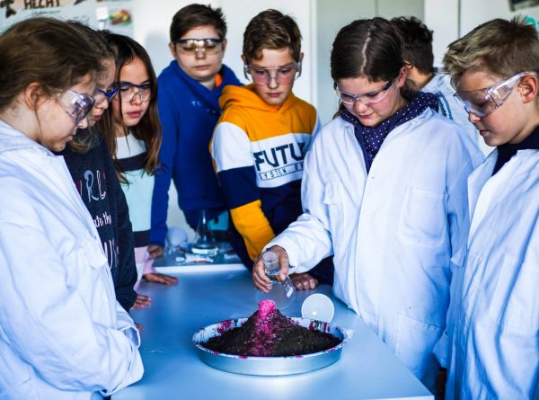Schüler stehen in Laborkitteln um ein Gefäß